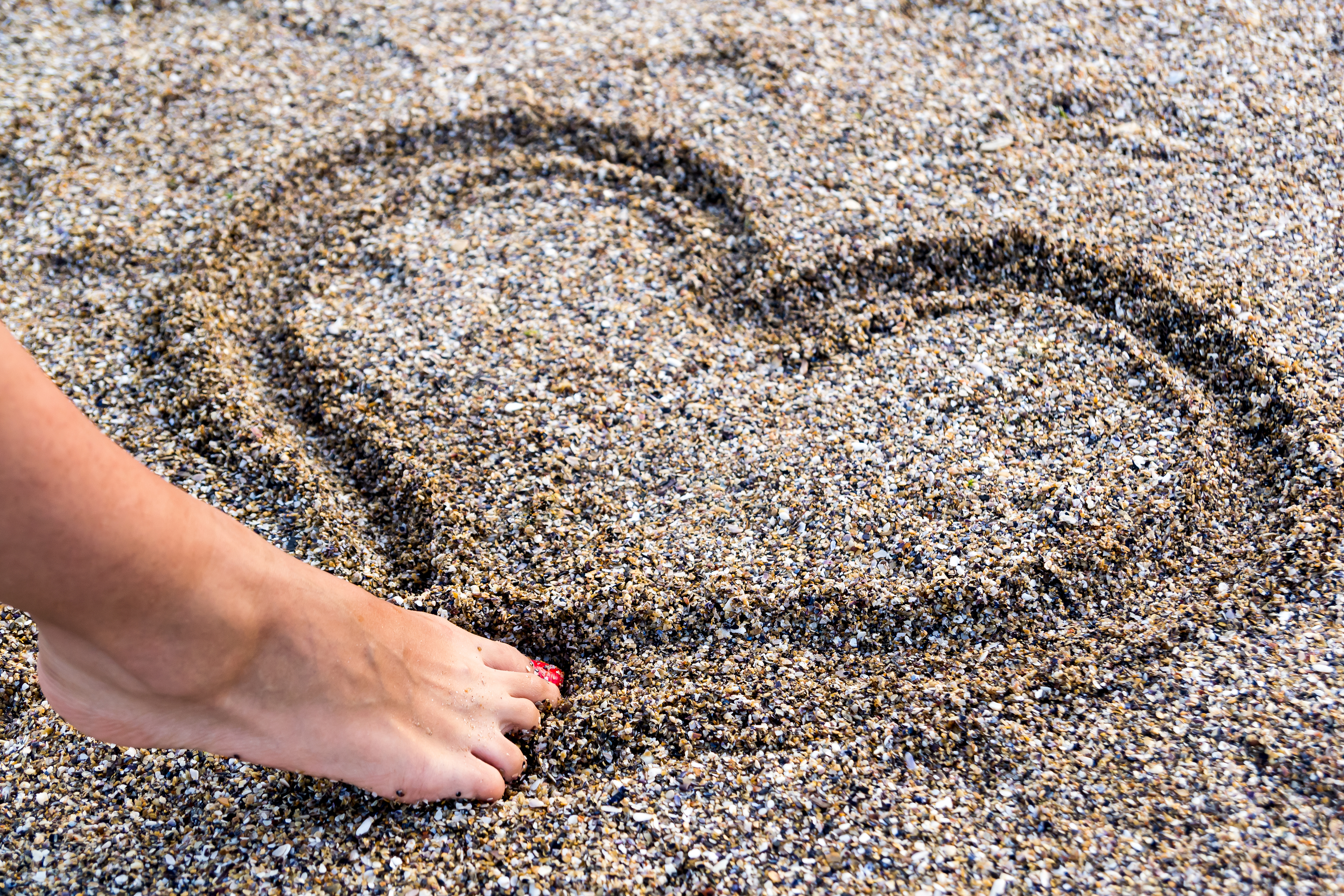 Девушка рисует сердце на песке